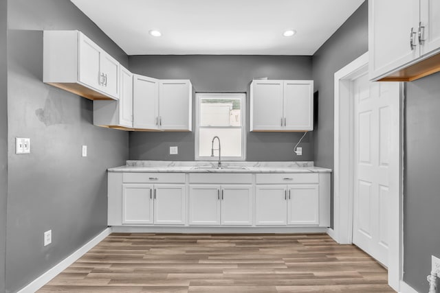 kitchen with sink, light stone counters, white cabinetry, and light hardwood / wood-style floors