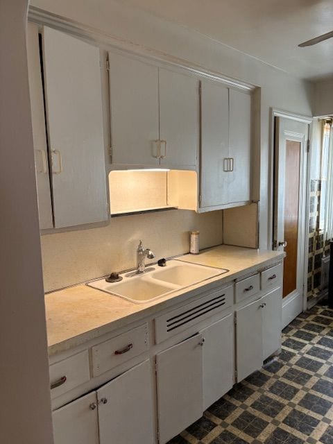 kitchen with a sink, light countertops, white cabinets, and ceiling fan
