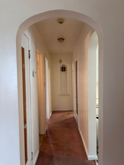 hall featuring carpet floors, baseboards, and arched walkways