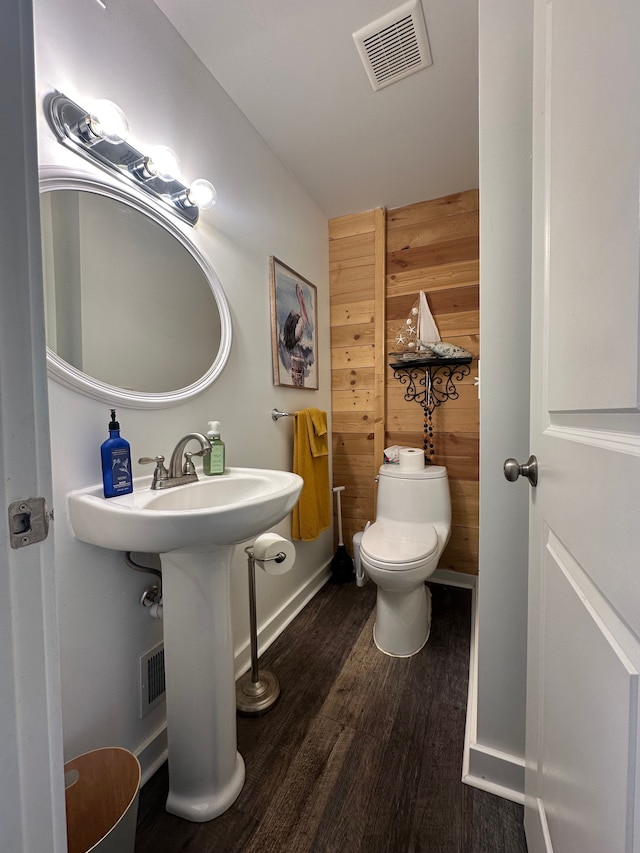 half bathroom with wooden walls, wood finished floors, visible vents, toilet, and baseboards