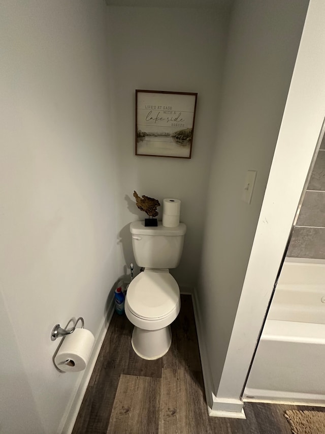 full bathroom with a tub to relax in, wood finished floors, toilet, and baseboards