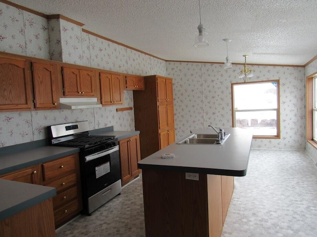 kitchen with decorative light fixtures, sink, crown molding, an island with sink, and stainless steel gas range