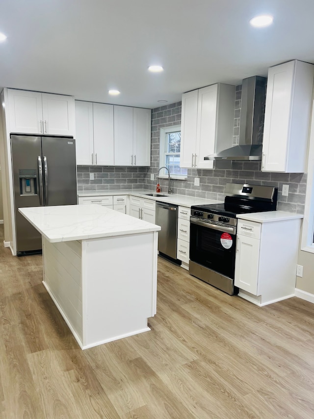 kitchen with light hardwood / wood-style floors, white cabinets, wall chimney range hood, and appliances with stainless steel finishes