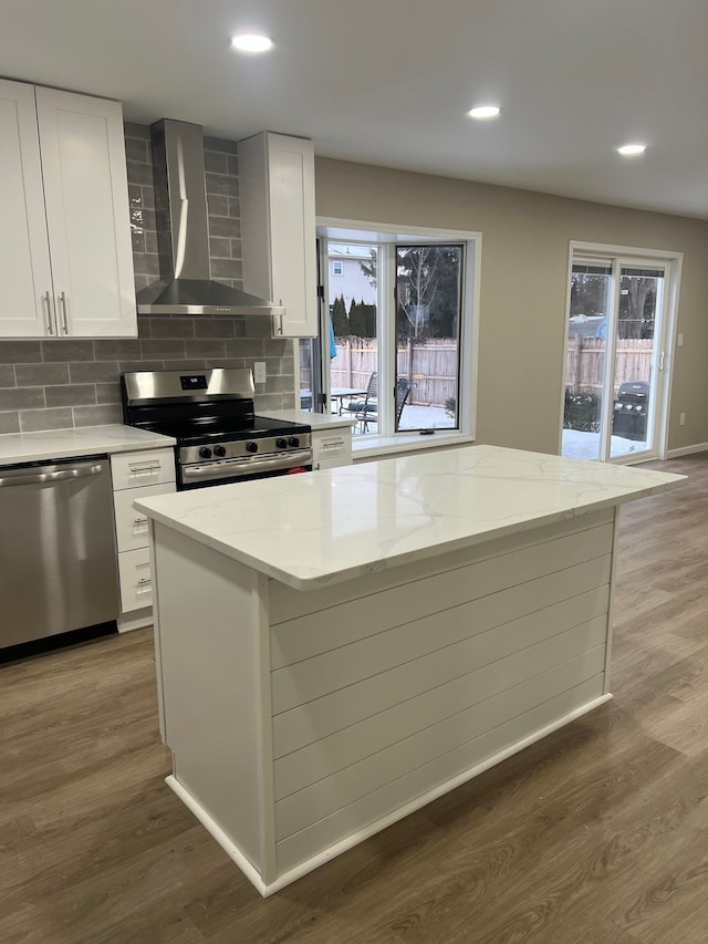 kitchen featuring white cabinetry, appliances with stainless steel finishes, light stone countertops, wall chimney exhaust hood, and a center island