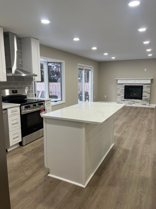 kitchen with electric range, white cabinets, a kitchen island, wall chimney exhaust hood, and light stone counters