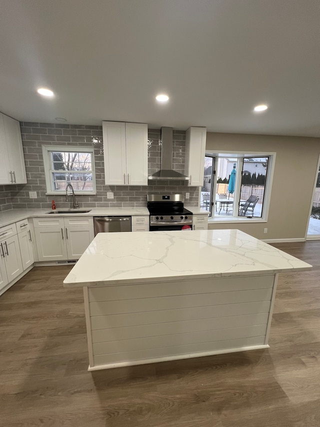 kitchen featuring white cabinetry, appliances with stainless steel finishes, wall chimney exhaust hood, light stone counters, and sink