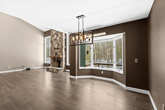 unfurnished dining area with lofted ceiling, a stone fireplace, a wealth of natural light, and a chandelier