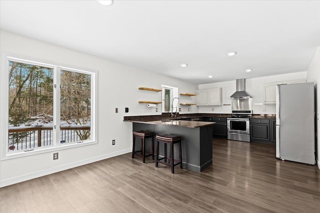 kitchen featuring appliances with stainless steel finishes, sink, a kitchen bar, kitchen peninsula, and wall chimney range hood