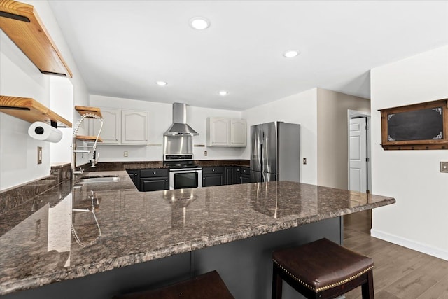 kitchen with dark hardwood / wood-style floors, a kitchen bar, kitchen peninsula, stainless steel appliances, and wall chimney range hood