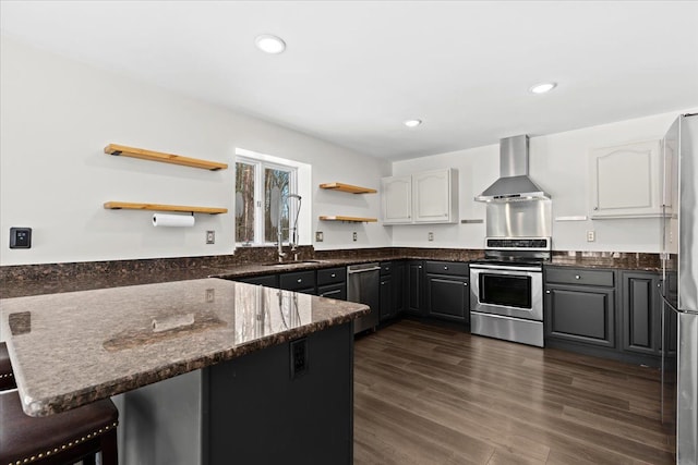 kitchen featuring appliances with stainless steel finishes, wall chimney range hood, white cabinets, and kitchen peninsula