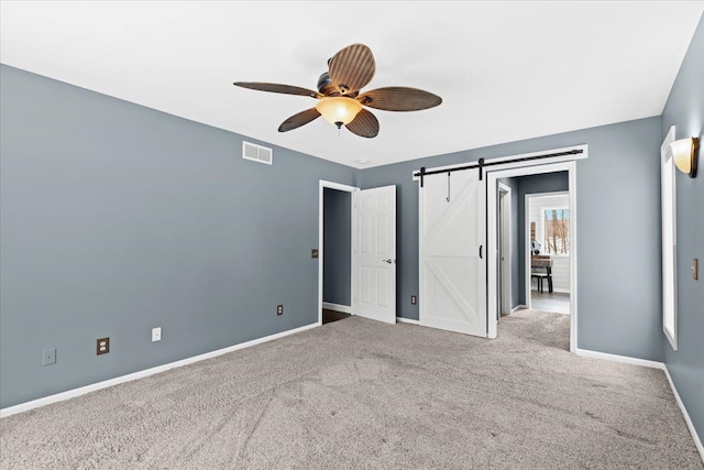 unfurnished bedroom featuring a barn door, carpet, and ceiling fan