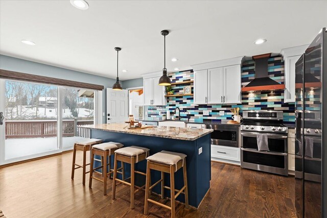 kitchen featuring white cabinets, wall chimney exhaust hood, a kitchen island, stainless steel appliances, and light stone counters