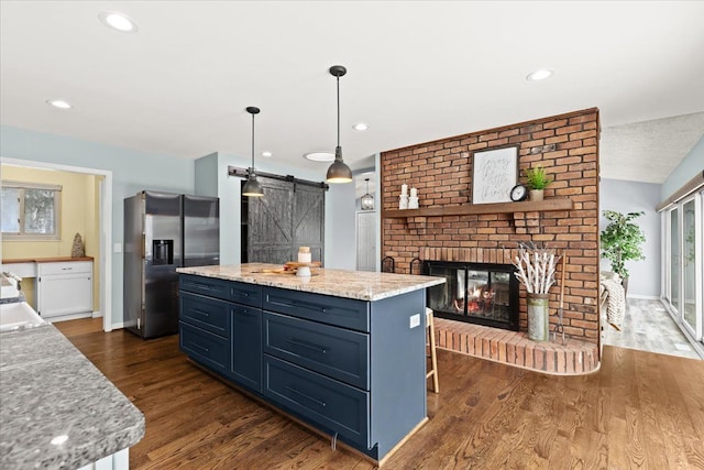 kitchen with stainless steel fridge with ice dispenser, a barn door, dark hardwood / wood-style flooring, hanging light fixtures, and a kitchen island