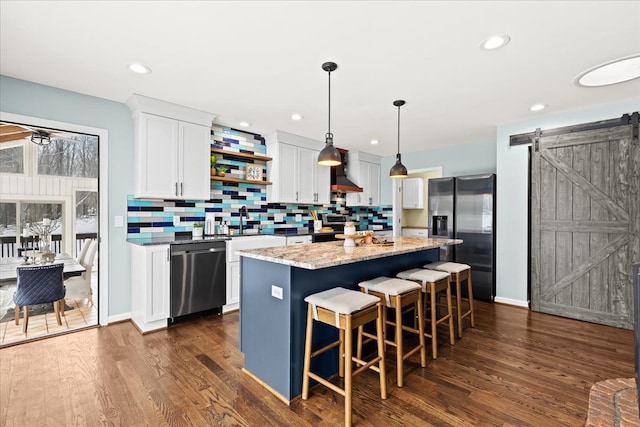 kitchen with appliances with stainless steel finishes, custom exhaust hood, a kitchen island, white cabinetry, and a barn door