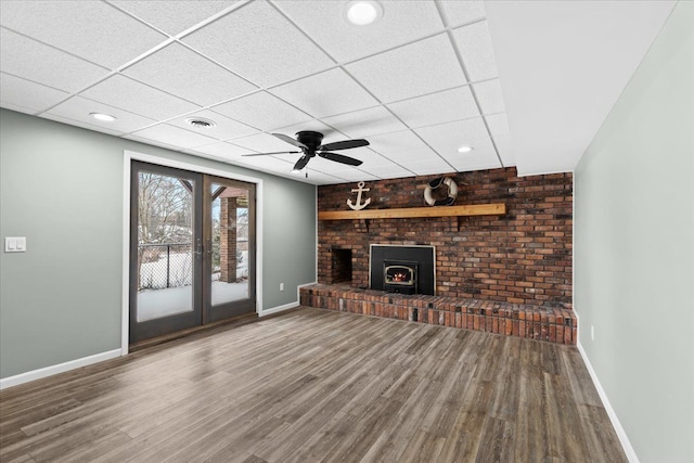 unfurnished living room with ceiling fan, a wood stove, wood-type flooring, and a paneled ceiling