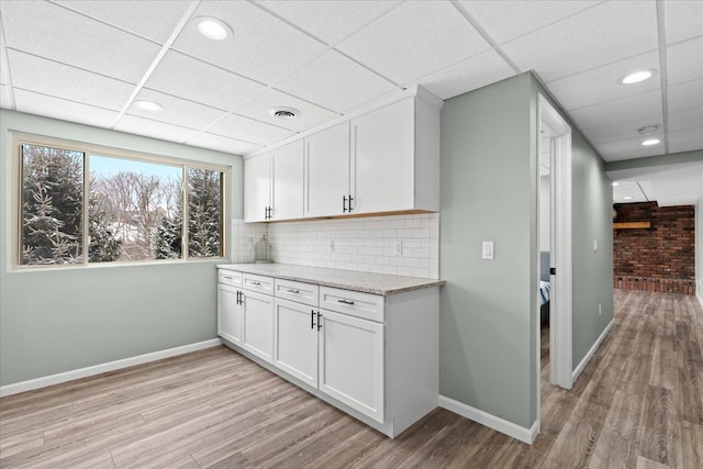 kitchen featuring decorative backsplash, white cabinetry, a paneled ceiling, and light wood-type flooring