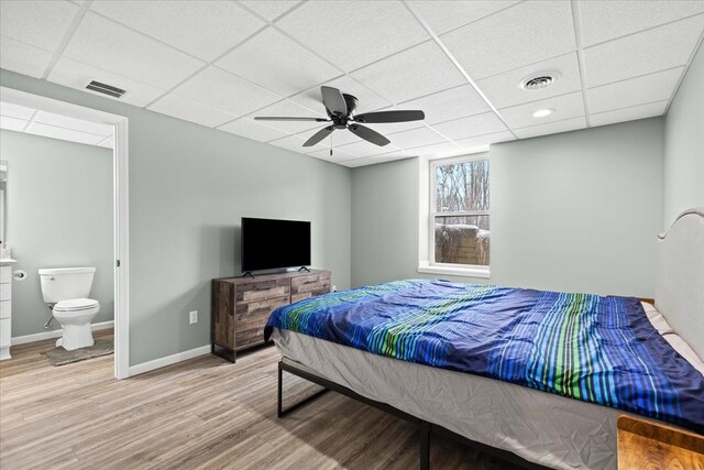 bedroom with ceiling fan, connected bathroom, a paneled ceiling, and hardwood / wood-style floors