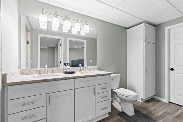 bathroom with toilet, vanity, a drop ceiling, and hardwood / wood-style floors