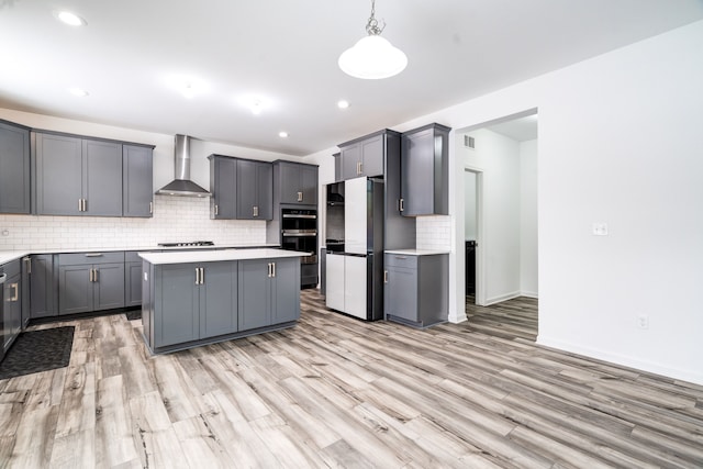 kitchen with wall chimney range hood, a center island, pendant lighting, gray cabinetry, and stainless steel fridge