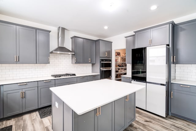 kitchen featuring gray cabinetry, wall chimney exhaust hood, refrigerator, and stainless steel gas stovetop