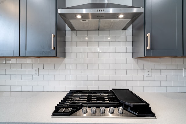 kitchen featuring exhaust hood, backsplash, gray cabinetry, and stainless steel gas stovetop