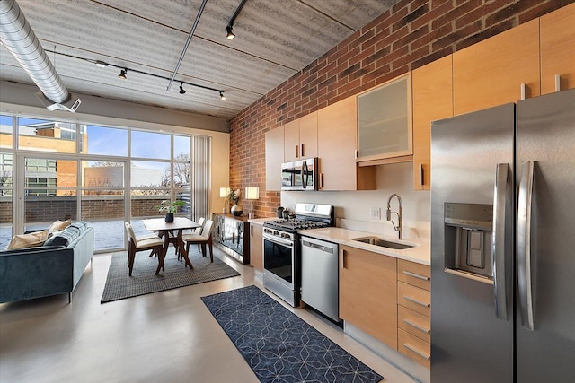 kitchen with brick wall, sink, stainless steel appliances, and rail lighting