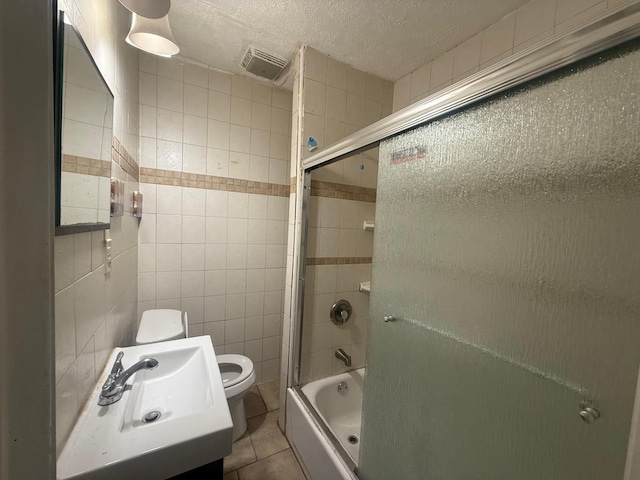 full bathroom with a textured ceiling, tile patterned flooring, bath / shower combo with glass door, toilet, and tile walls