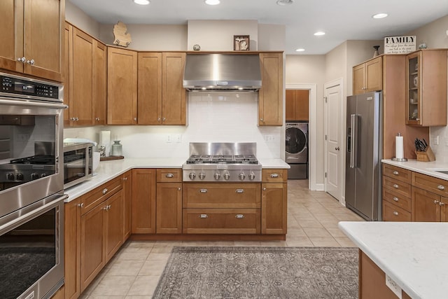 kitchen featuring appliances with stainless steel finishes, wall chimney exhaust hood, washer / clothes dryer, decorative backsplash, and light tile patterned floors