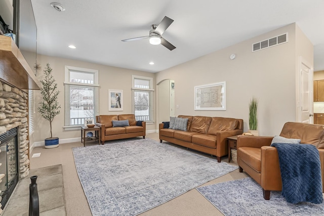 living room featuring ceiling fan, light carpet, and a stone fireplace