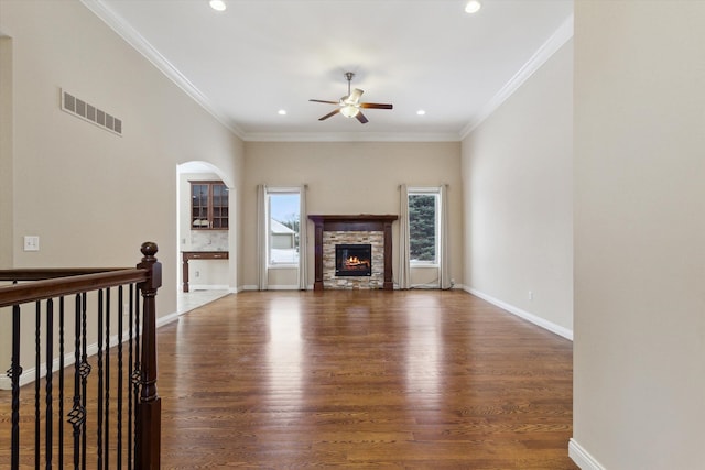 unfurnished living room with dark wood-type flooring, crown molding, a stone fireplace, and ceiling fan