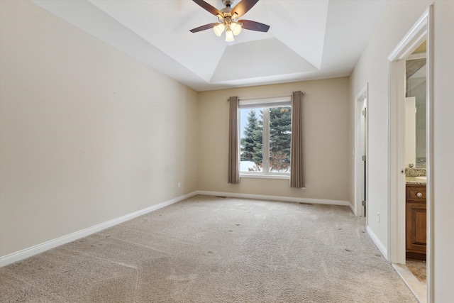 unfurnished bedroom featuring ceiling fan, light colored carpet, a tray ceiling, and ensuite bath