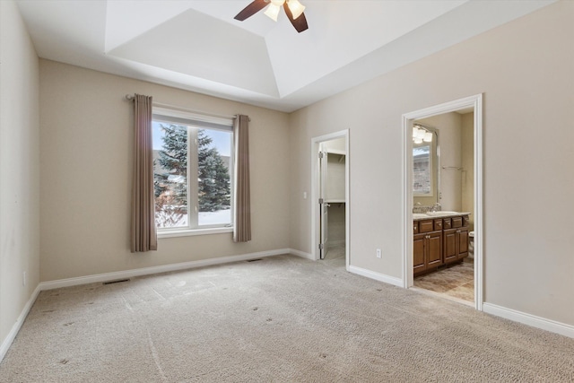 unfurnished bedroom featuring ceiling fan, light colored carpet, a raised ceiling, a spacious closet, and connected bathroom