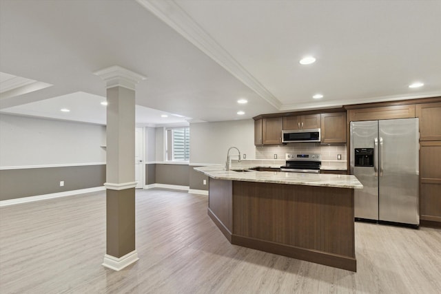 kitchen featuring an island with sink, appliances with stainless steel finishes, light stone countertops, ornamental molding, and sink