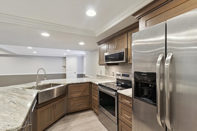 kitchen featuring kitchen peninsula, sink, appliances with stainless steel finishes, ornamental molding, and light stone counters