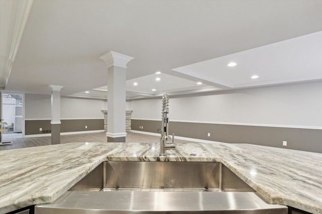 interior details featuring decorative columns, sink, ornamental molding, and light stone countertops