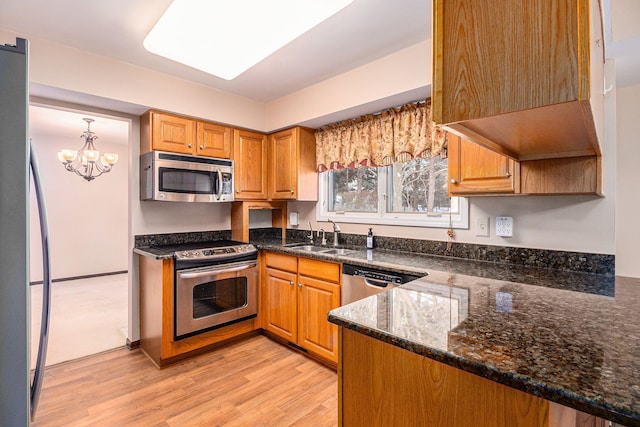 kitchen featuring dark stone countertops, appliances with stainless steel finishes, sink, light wood-type flooring, and kitchen peninsula