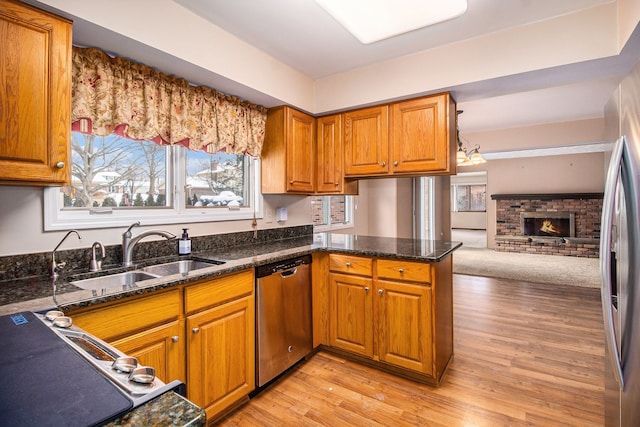 kitchen featuring appliances with stainless steel finishes, sink, dark stone counters, light hardwood / wood-style floors, and kitchen peninsula