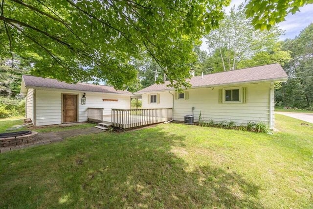 rear view of house with cooling unit, a deck, and a lawn