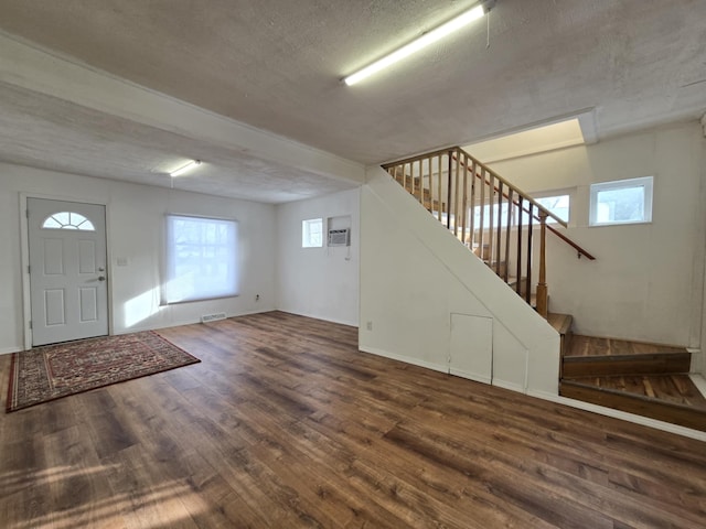 foyer entrance featuring a healthy amount of sunlight, dark wood-type flooring, a textured ceiling, and a wall mounted air conditioner