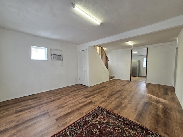 basement with a wall unit AC, stainless steel refrigerator, a textured ceiling, and hardwood / wood-style floors