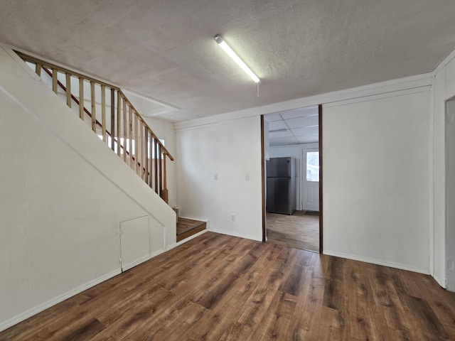 basement featuring dark wood-type flooring, a textured ceiling, and black fridge