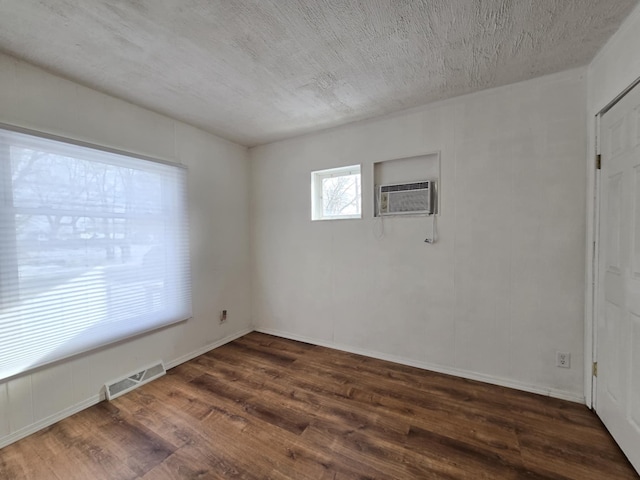 empty room featuring a textured ceiling, dark wood-type flooring, and a wall mounted AC