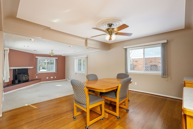 dining area with ceiling fan, a wood stove, and wood-type flooring