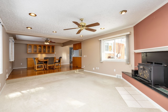 carpeted living room featuring ceiling fan, a wood stove, a textured ceiling, and ornamental molding