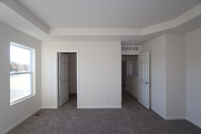 unfurnished bedroom with a spacious closet, a closet, dark carpet, and a tray ceiling