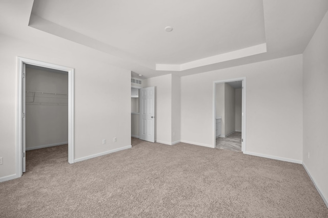 unfurnished bedroom with a tray ceiling, a walk in closet, light colored carpet, and a closet