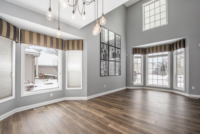 empty room with a high ceiling, wood finished floors, visible vents, and baseboards