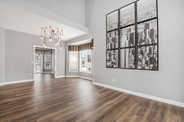 unfurnished room featuring a notable chandelier, wood finished floors, and baseboards