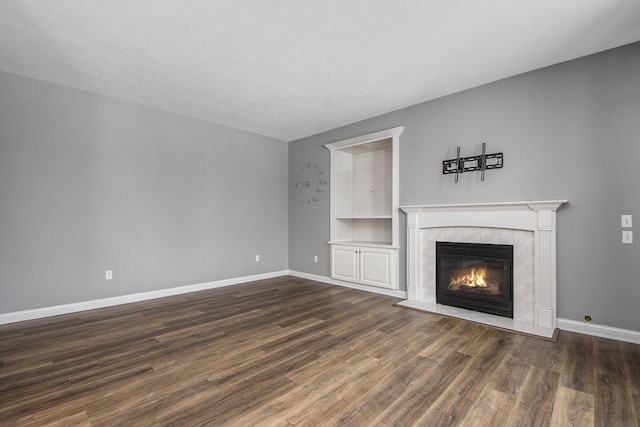 unfurnished living room with dark wood-style flooring, baseboards, and a tiled fireplace