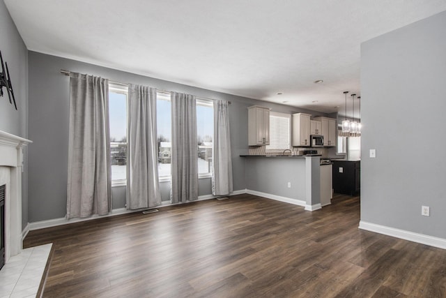 unfurnished living room with dark wood-style floors, a sink, a tile fireplace, and baseboards